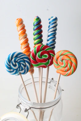 Brightly wrapped lollipops standing upright in a glass jar.
