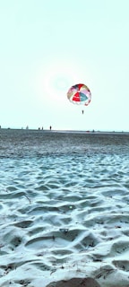 Crowd on the beach looking up at a paramotor carrying a colorful promotional banner.