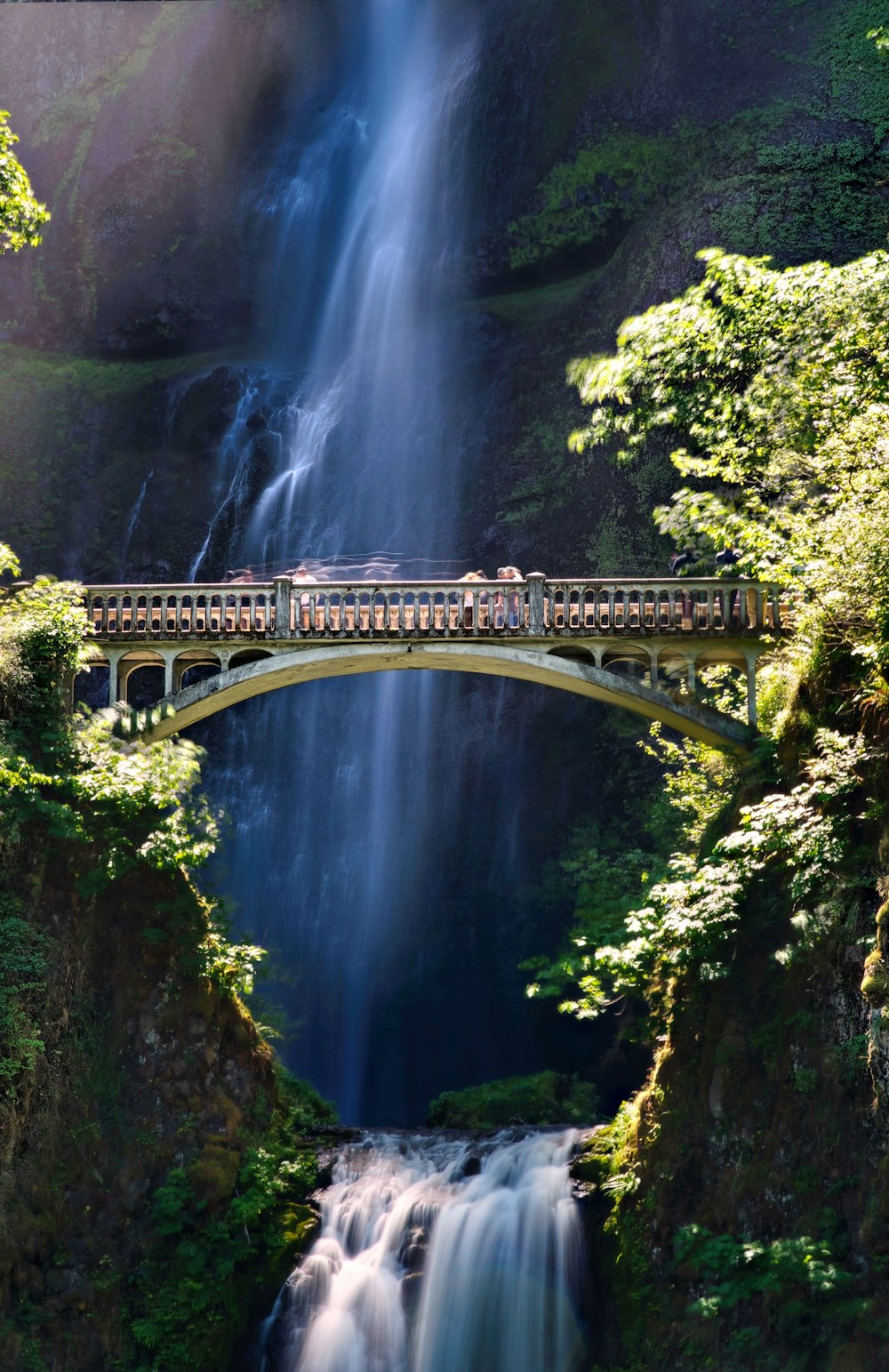 a bridge over a waterfall with a waterfall in the background