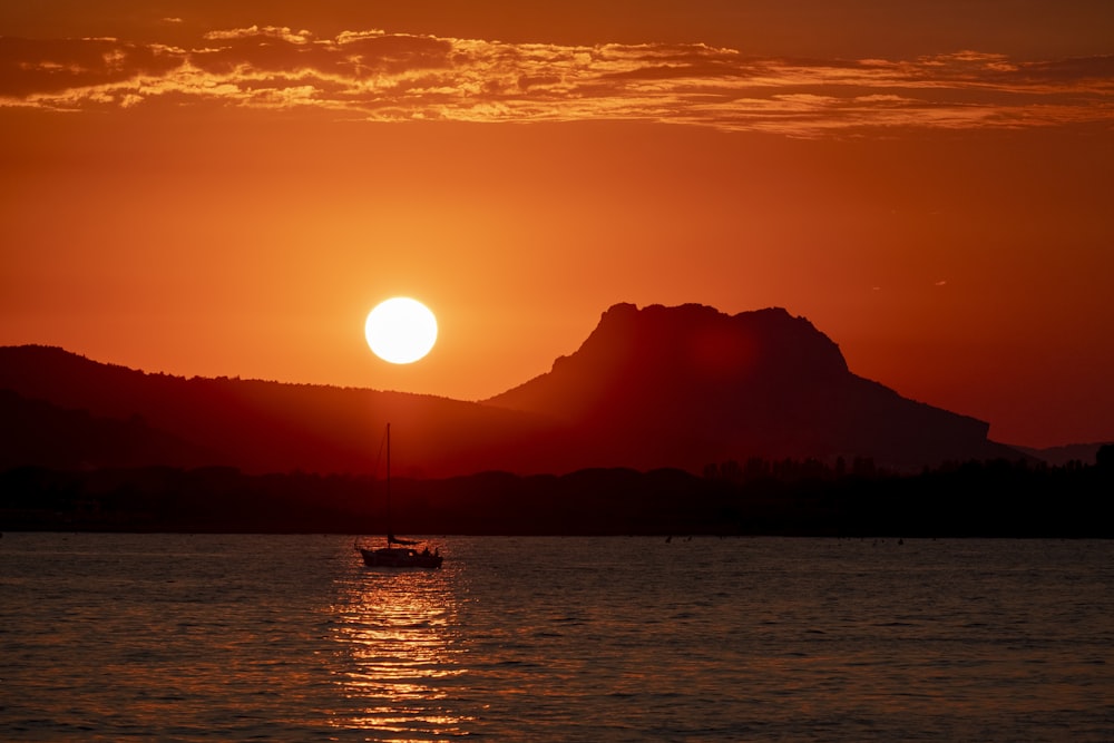 the sun is setting over a mountain and a boat is in the water