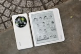 A Xiaomi smartphone and a Kobo e-reader are placed side by side on a concrete surface. The smartphone features a prominent camera module, and the e-reader displays a page from a manga comic strip. The background consists of a textured, stone-like surface.