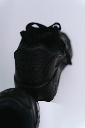 Close-up of sleek black premium sneakers with gold accents on a minimalist white background.