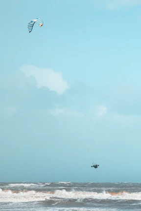 Kite surfer catching air against a bright blue sky over the waves