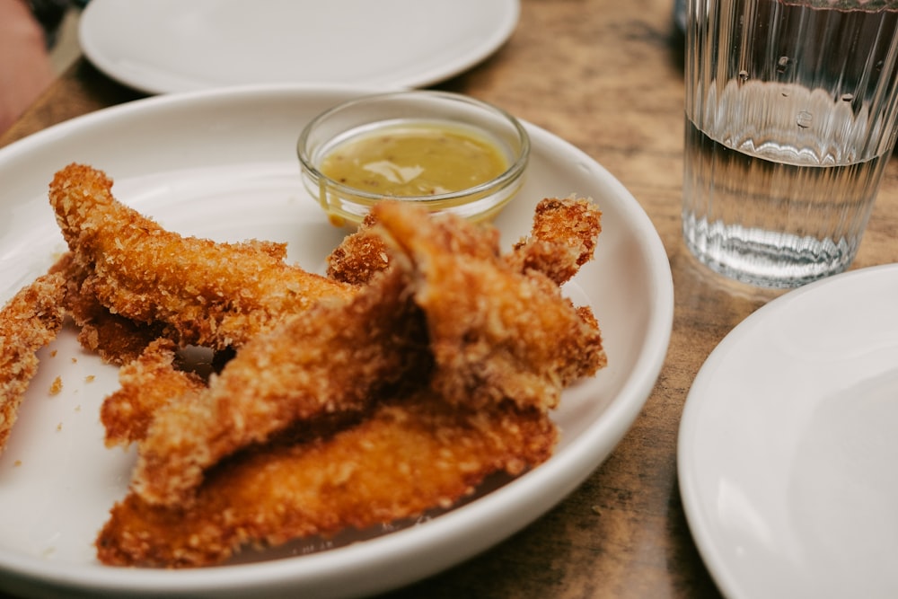 a white plate topped with fried food next to a glass of water