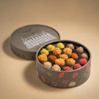 An elegant box of assorted truffles with vibrant colors and glossy finishes arranged on a marble countertop.