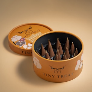 A round, decorative box with floral designs on the lid and sides, containing a neatly arranged set of cone-shaped chocolates with golden tips. The box is open, revealing the interior with chocolates placed in individual compartments.
