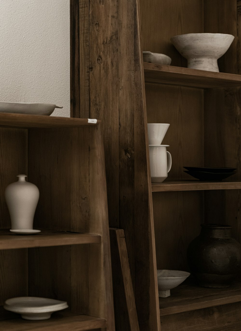 a wooden shelf filled with white dishes and vases