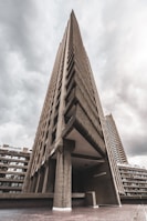 A towering concrete structure with an imposing, brutalist architectural style. The sharp angles and textured facade are highlighted against a backdrop of overcast skies, lending a dramatic feel to the scene.