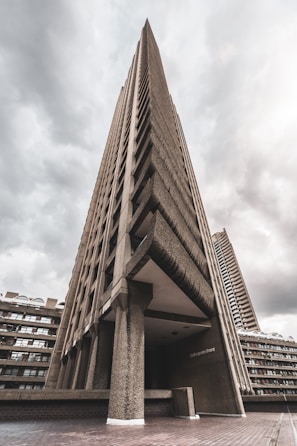 A towering concrete structure with an imposing, brutalist architectural style. The sharp angles and textured facade are highlighted against a backdrop of overcast skies, lending a dramatic feel to the scene.