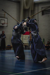 Kendo practitioners in traditional gear practicing strikes in a dojo bathed in natural light.