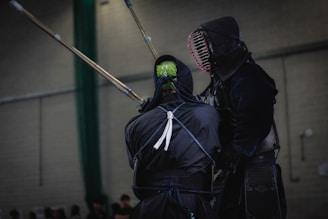 Two individuals are engaged in a kendo match, with protective gear and bamboo swords. The setting appears to be indoors, possibly in a gym with a neutral color palette.