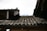 A close-up view of a weathered, tiled roof with dark, textured tiles. There is a pipe protruding from the structure, and dry leaves and debris are scattered across the tiles. The roof shows signs of aging and exposure to the elements, with some spots appearing mossy or worn.