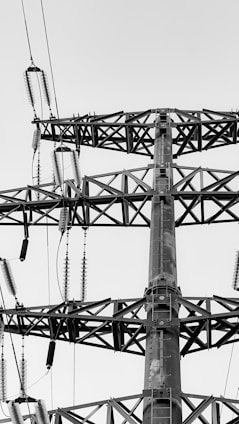 A high-voltage transmission tower is prominently featured, with intricate metal framework and insulators extending from the structure. The monochrome color palette highlights the geometric design and functional components such as cables and support bars.
