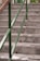 Marble stairs with a green metal handrail, offering a contrast between the smooth texture of the stone and the vibrant metallic color. A few small brown objects are scattered on the steps, and a glimpse of greenery is visible at the top, suggesting an indoor or garden setting.