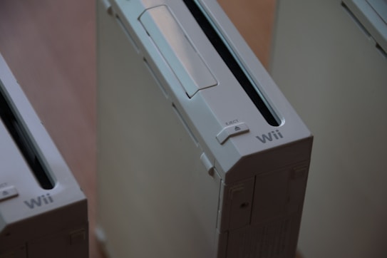 A close-up view of multiple white gaming consoles with a sleek design and an 'eject' button visible. The brand name 'Wii' is prominently displayed.