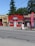 A small massage parlor with a bright red facade is located along a street. It features a prominent blue and white sign with the word 'MASSAGE' above the entrance. There is a large red vertical banner with the same word on the sidewalk. Several potted plants and decorations are placed near the door.