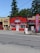 A small massage parlor with a bright red facade is located along a street. It features a prominent blue and white sign with the word 'MASSAGE' above the entrance. There is a large red vertical banner with the same word on the sidewalk. Several potted plants and decorations are placed near the door.