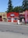 A small massage parlor with a bright red facade is located along a street. It features a prominent blue and white sign with the word 'MASSAGE' above the entrance. There is a large red vertical banner with the same word on the sidewalk. Several potted plants and decorations are placed near the door.