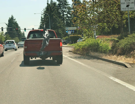 Red and black pickup truck speeding down highway with trailer in tow under a clear sky.