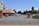 A Mexican-style restaurant with a red tile roof is situated next to a parking lot with several cars parked. The sign outside displays the restaurant's name and mentions margaritas to go. Surrounding the area are trees and bushes with a clear blue sky in the background.