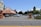 A Mexican-style restaurant with a red tile roof is situated next to a parking lot with several cars parked. The sign outside displays the restaurant's name and mentions margaritas to go. Surrounding the area are trees and bushes with a clear blue sky in the background.