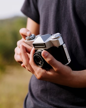 Hands holding a vintage film camera with blurred background.