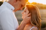 A romantic moment between a man and a woman, with the man gently holding the woman's face as they stand close together under a warm, glowing sunset.