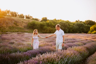 A romantic couple holding hands in a garden bathed in soft lilac light at sunset.