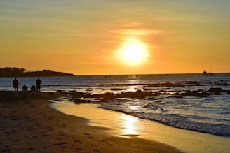 A golden sunset over the calm Gulf Coast waters with a family walking along the shore.