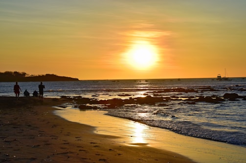 A golden sunset over the calm Gulf Coast waters with a family walking along the shore.
