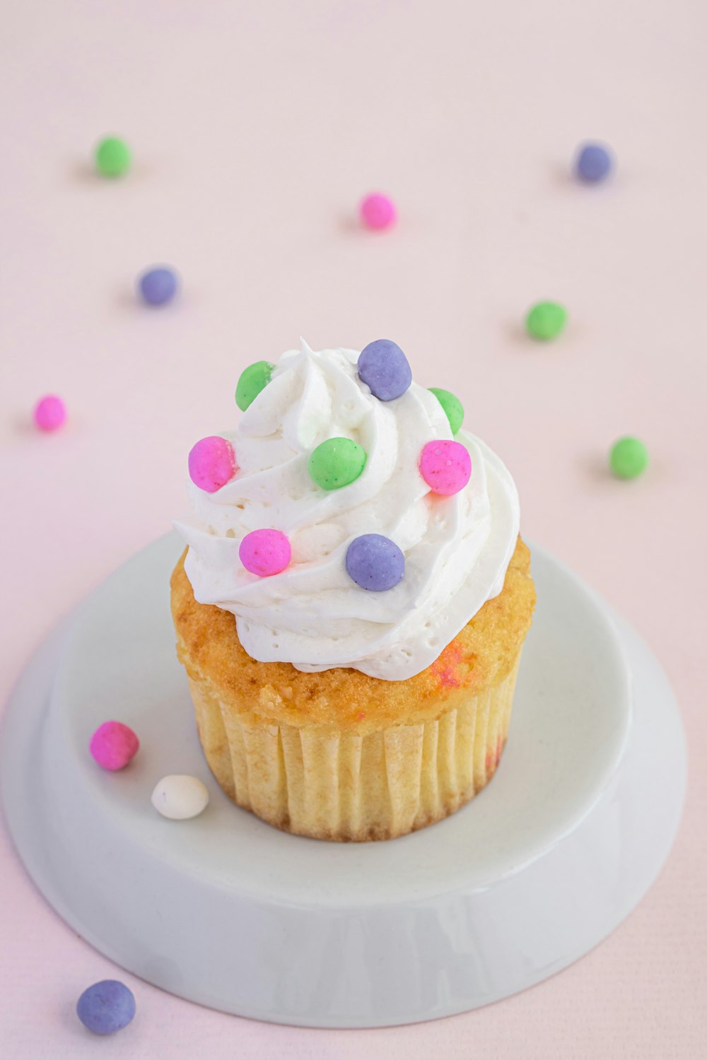 a cupcake with white frosting and sprinkles on a plate