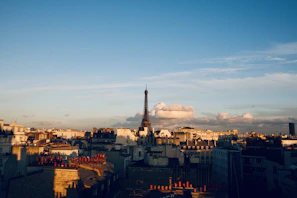 A panoramic sunset view of Paris with the Eiffel Tower silhouetted against the warm sky.