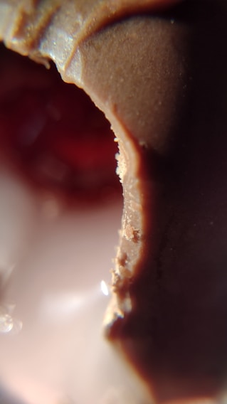 Close-up of a handcrafted chocolate piece with delicate gold leaf accents on a pearl white background.