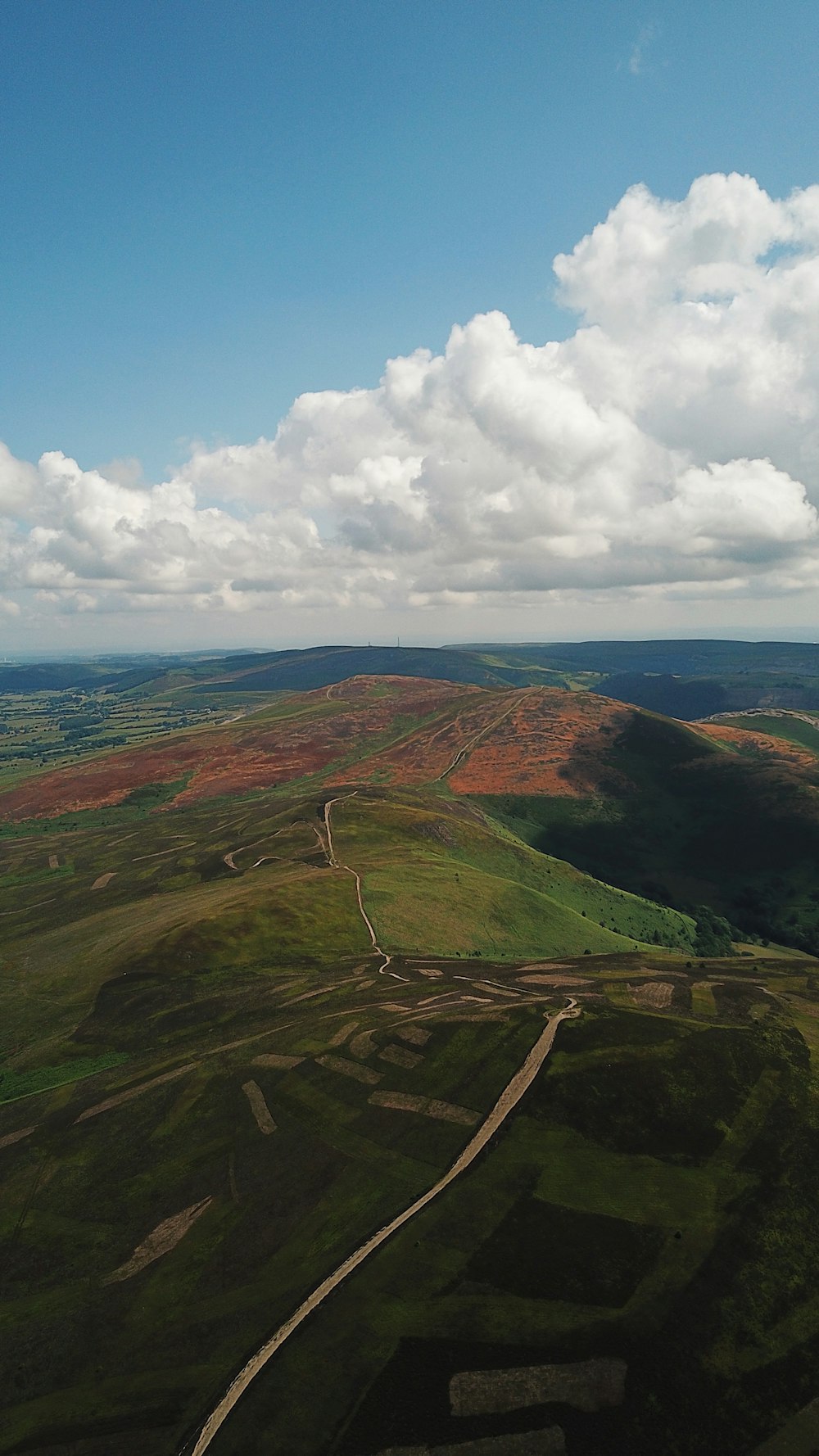 a plane flying over a lush green hillside under a cloudy blue sky