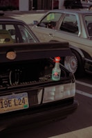 A parked car with an open trunk displaying a bottle of ceramic speed shine placed on the edge of the trunk. The car has a South Dakota license plate. Another vehicle is situated beside it, partially visible in the frame.