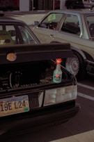 A parked car with an open trunk displaying a bottle of ceramic speed shine placed on the edge of the trunk. The car has a South Dakota license plate. Another vehicle is situated beside it, partially visible in the frame.