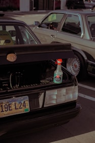 A parked car with an open trunk displaying a bottle of ceramic speed shine placed on the edge of the trunk. The car has a South Dakota license plate. Another vehicle is situated beside it, partially visible in the frame.