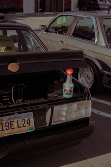 A parked car with an open trunk displaying a bottle of ceramic speed shine placed on the edge of the trunk. The car has a South Dakota license plate. Another vehicle is situated beside it, partially visible in the frame.