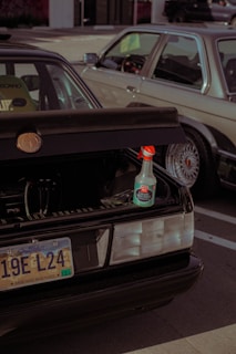 A parked car with an open trunk displaying a bottle of ceramic speed shine placed on the edge of the trunk. The car has a South Dakota license plate. Another vehicle is situated beside it, partially visible in the frame.