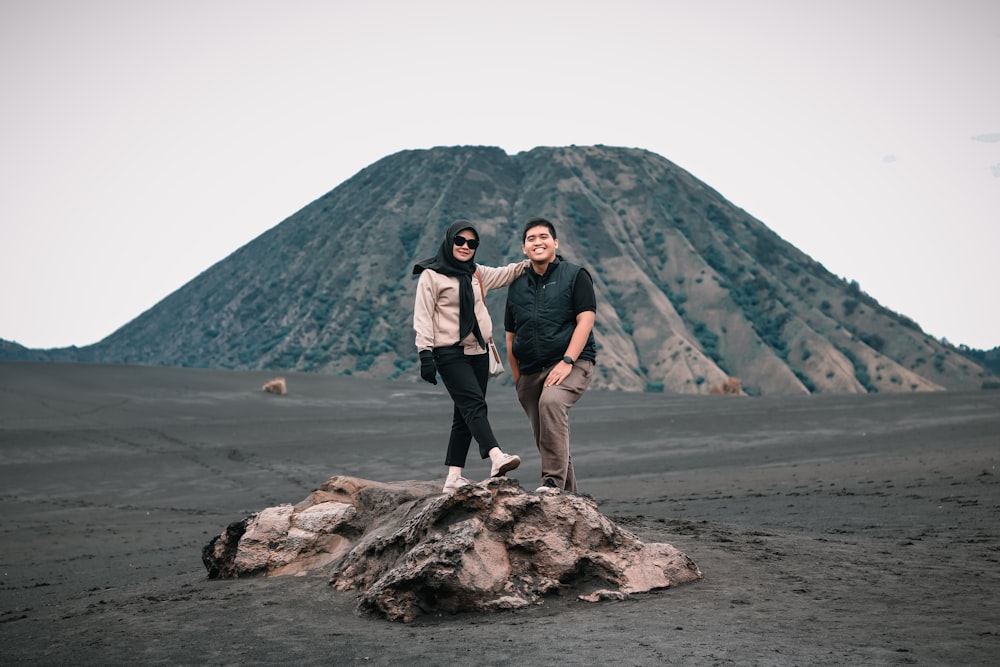 two people standing on a rock in front of a mountain