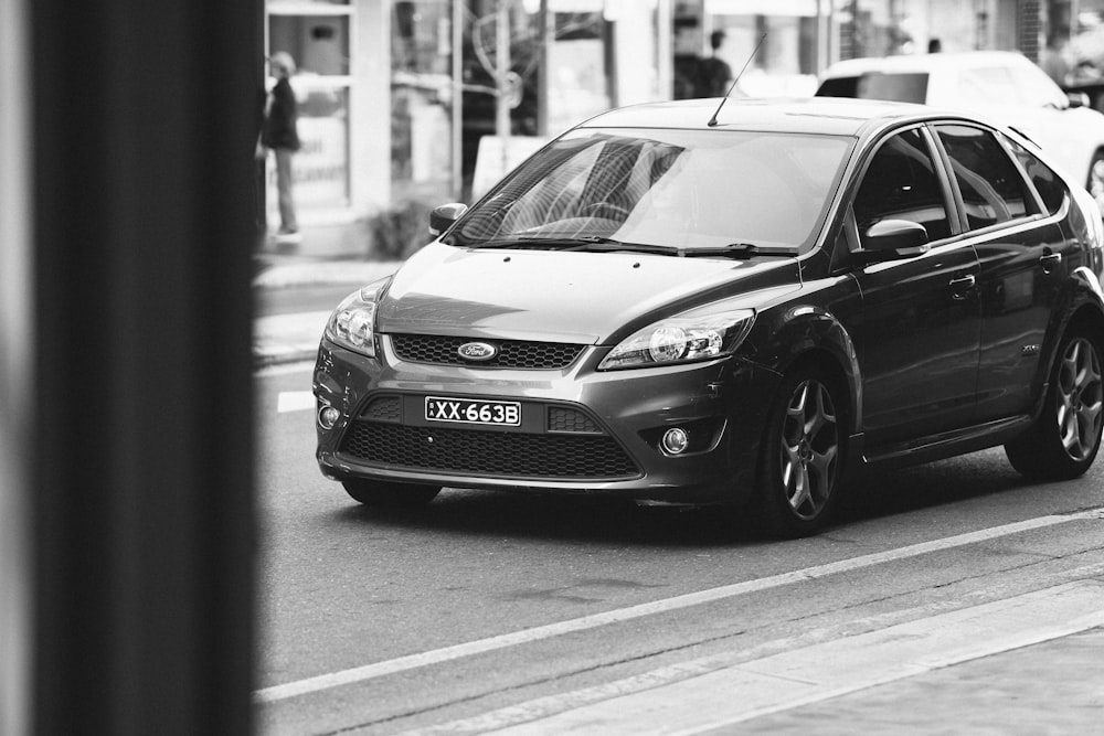 a black and white photo of a car driving down the street