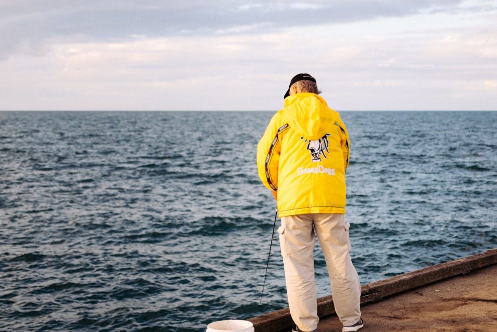 a man in a yellow jacket looking out at the ocean