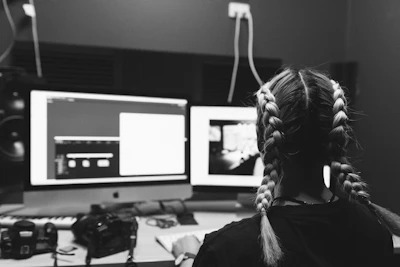 a woman sitting in front of two computer monitors