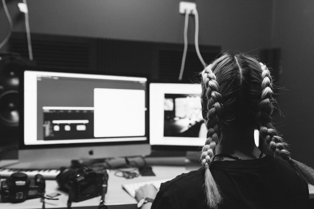 a woman sitting in front of two computer monitors