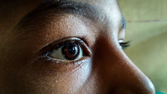 A close-up view of a person's eye with detailed focus on the texture of the skin and eyelashes. The image highlights the natural curvature and expression of the eye.