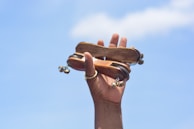 A hand is holding a traditional wooden musical instrument with several small bells attached. The object is being held up against a clear blue sky.