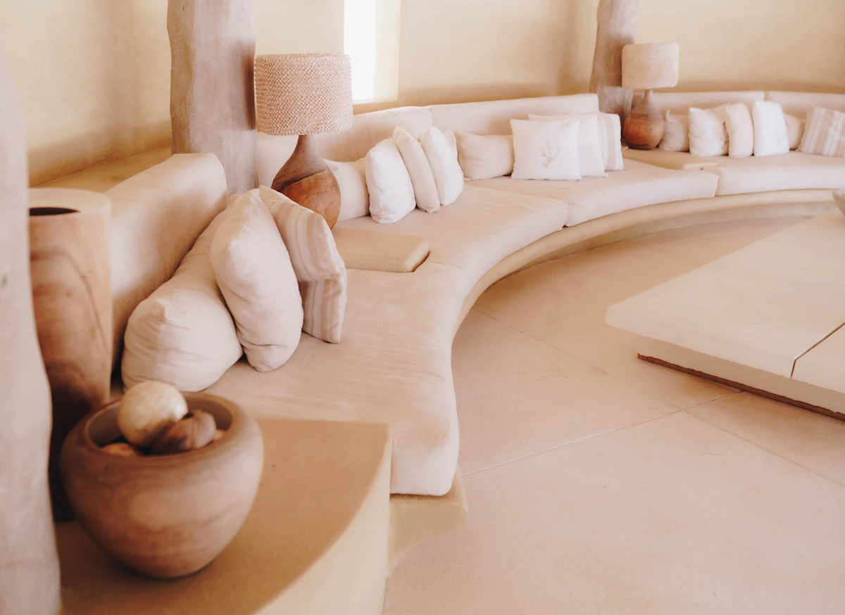 A curved plaster banquette heaped with linen cushions, a clay pot and a woven lamp