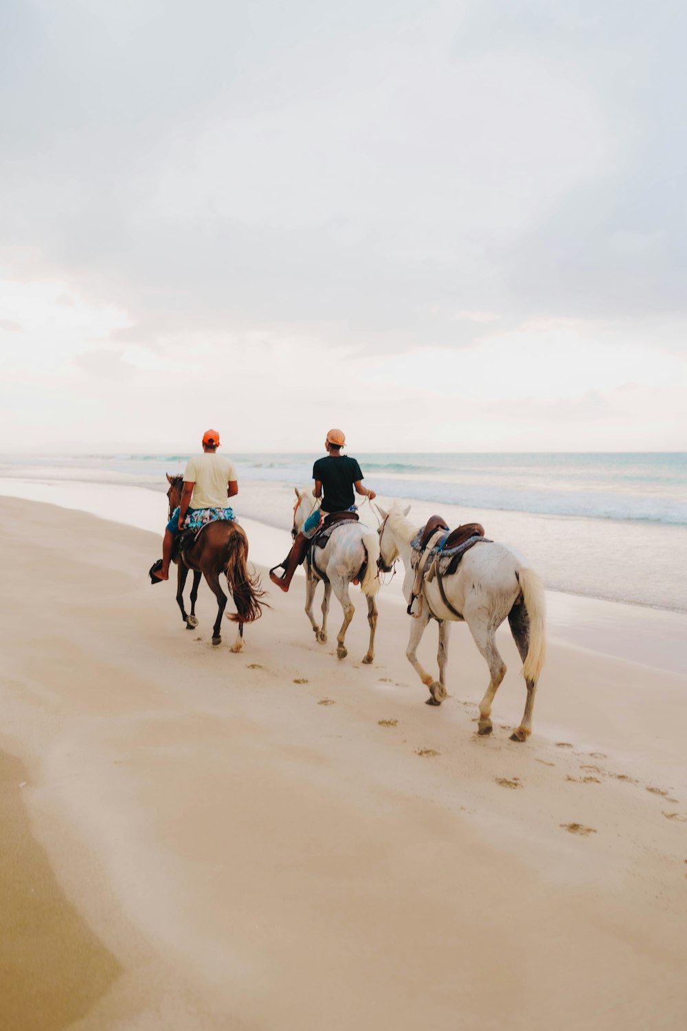 a group of people riding horses down a beach