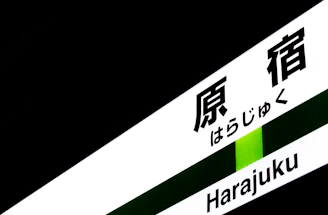 A sign containing both Japanese characters and Roman letters spelling 'Harajuku', set against a predominantly dark background with a green stripe.