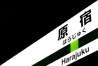 A sign containing both Japanese characters and Roman letters spelling 'Harajuku', set against a predominantly dark background with a green stripe.